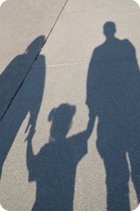 Shadow of two adults and one child holding hands on concrete outdoors